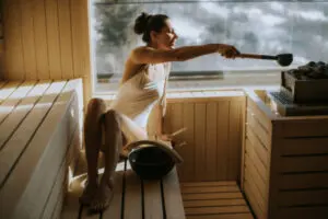 Woman poring water on sauna rocks with ladle in sauna