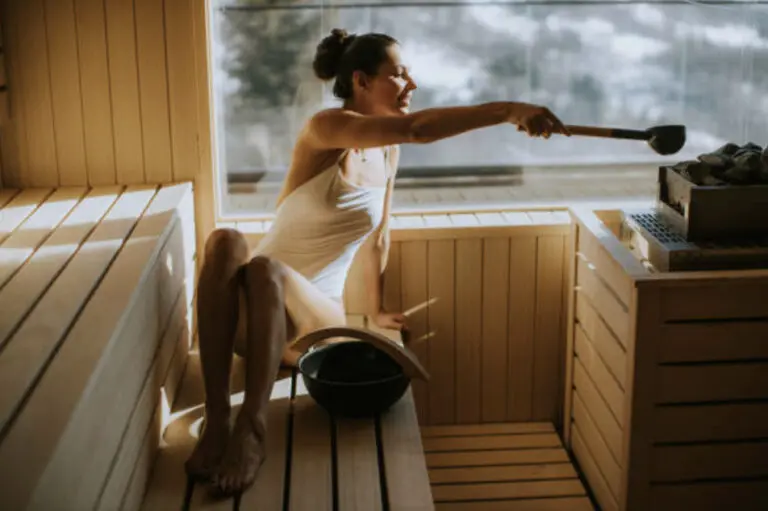 Woman poring water on sauna rocks with ladle in sauna